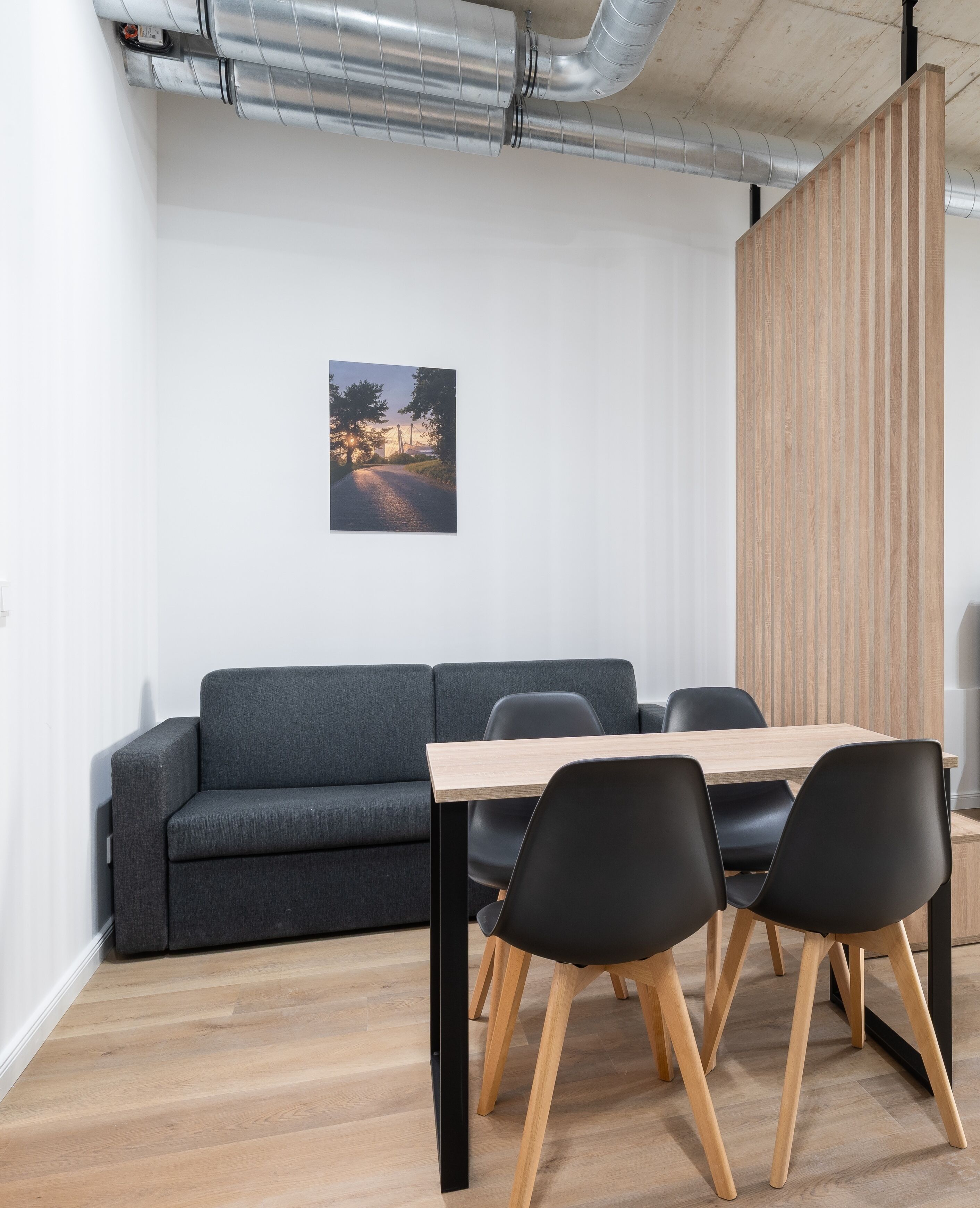 Une salle de réunion moderne avec une table en bois, des chaises noires, un canapé gris et un tableau encadré au mur.