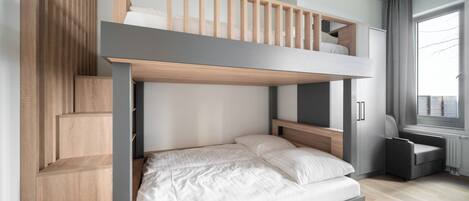 A bunk bed room with a wooden ladder, a desk, and a chair.