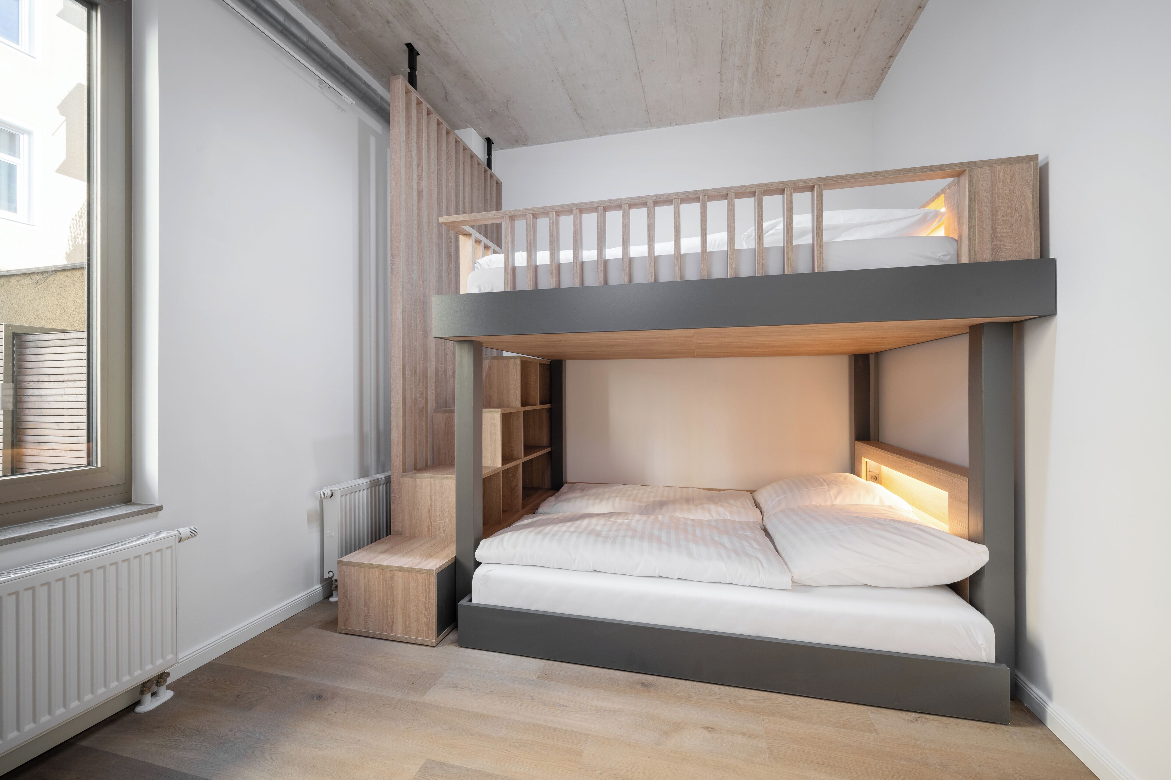 A bunk bed with a built-in desk and shelving, a radiator, and a window.