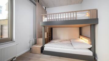 A bunk bed with a built-in desk and shelving, a radiator, and a window.
