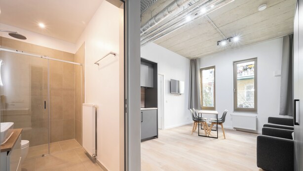 Un appartement moderne doté d’une douche en verre, d’un coin repas avec une table et des chaises, et d’une cuisine équipée d’un réfrigérateur et de placards.