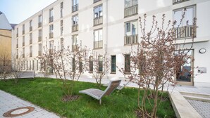 A modern building with multiple windows and balconies, a grassy area with benches, and a paved walkway. - Homaris Apartments Isartor (Munich)