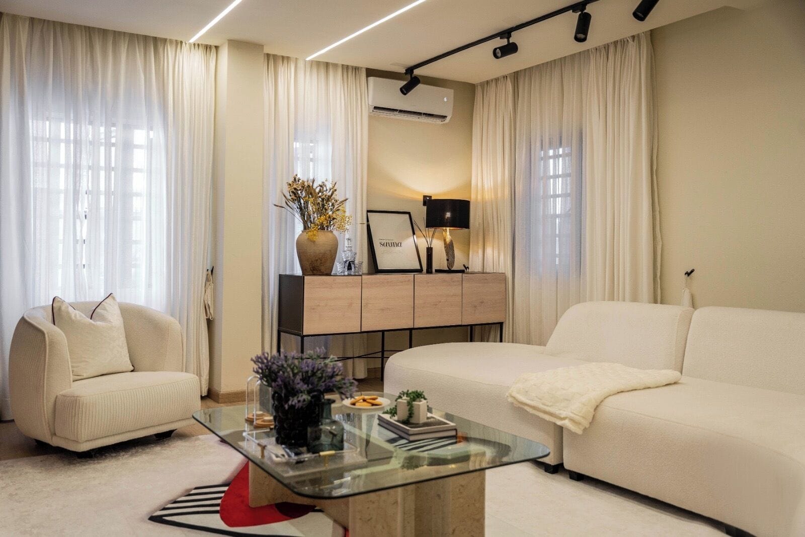 Una sala de estar moderna con una mesa de centro de vidrio, dos sofás, un mueble aparador y un televisor.