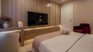 A modern hotel room with a large bed, a TV mounted on the wall, a red chair, and a bedside table with candles. - Libertini Apartments by FreedomWay (Lekki)