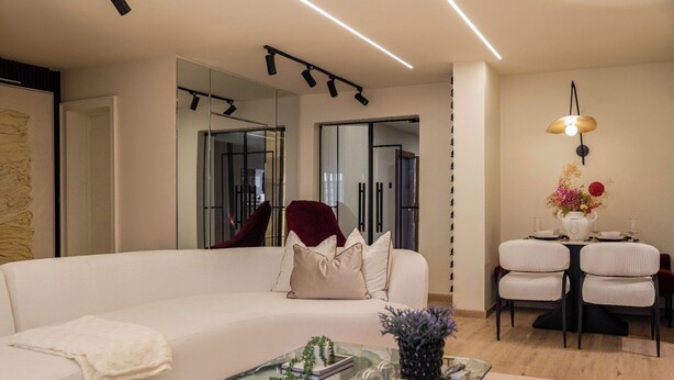 A modern living room with a white sofa, a glass coffee table, and a dining area with a white table and chairs. - Libertini Apartments by FreedomWay (Lekki)