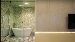 A modern bathroom with a freestanding bathtub, a glass shower enclosure, and a wall-mounted television. - Libertini Apartments by FreedomWay (Lekki)