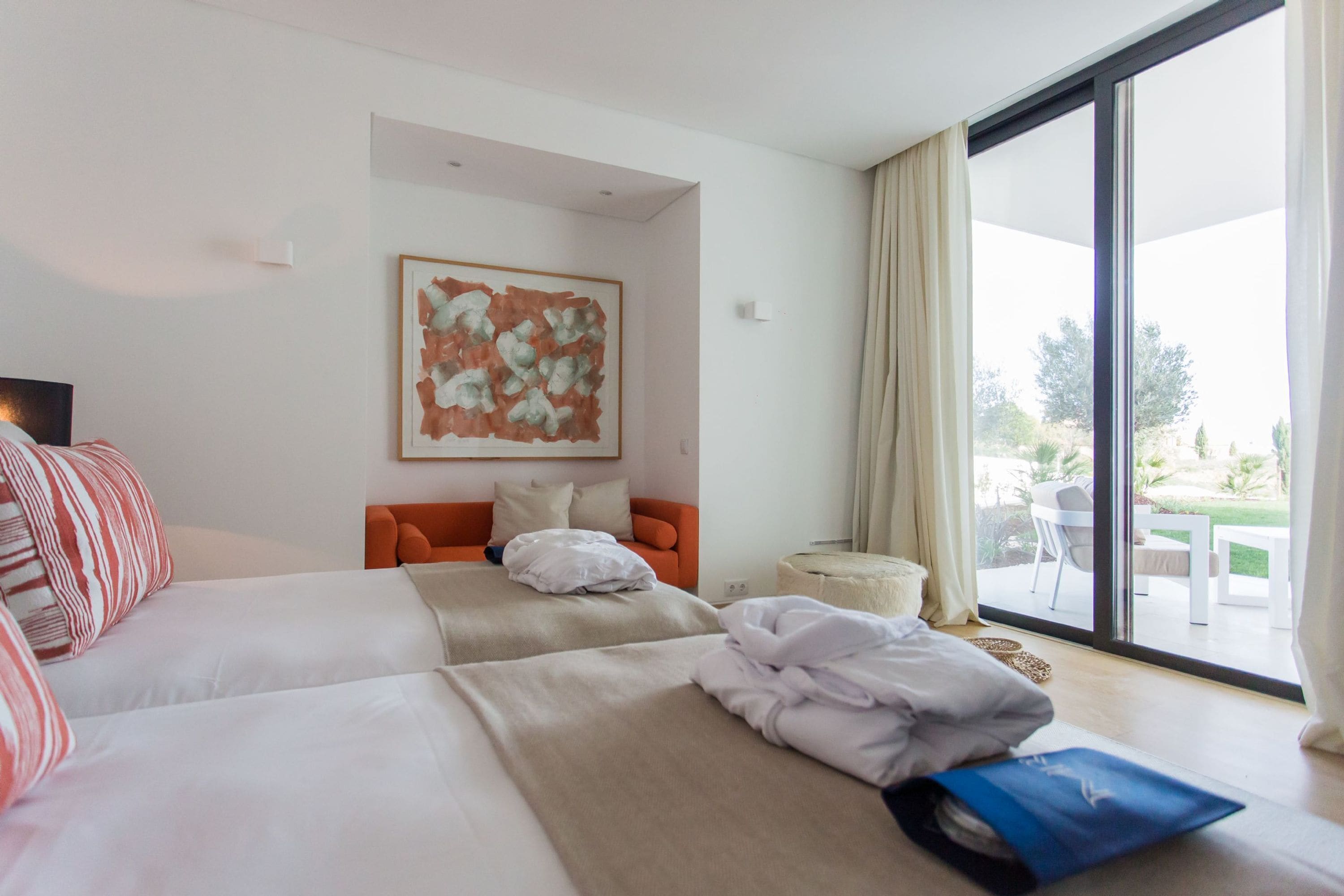 Een hotelkamer met twee bedden, een bank, een groot raam met uitzicht op de omgeving en een schilderij aan de muur.