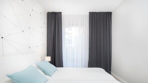 A modern hotel room with a white bed, two light blue pillows, a geometric wall design, and a window with sheer curtains. - City of the Kings-Milford Sound (Kraków)