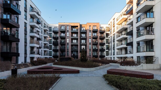 A modern apartment complex with multiple floors, balconies, and a central courtyard with seating areas. - City of the Kings-Milford Sound (Kraków)