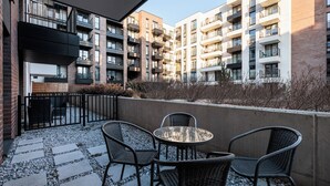 A modern apartment building with balconies, a patio area with chairs and a table, and a view of the surrounding area. - City of the Kings-Milford Sound (Kraków)