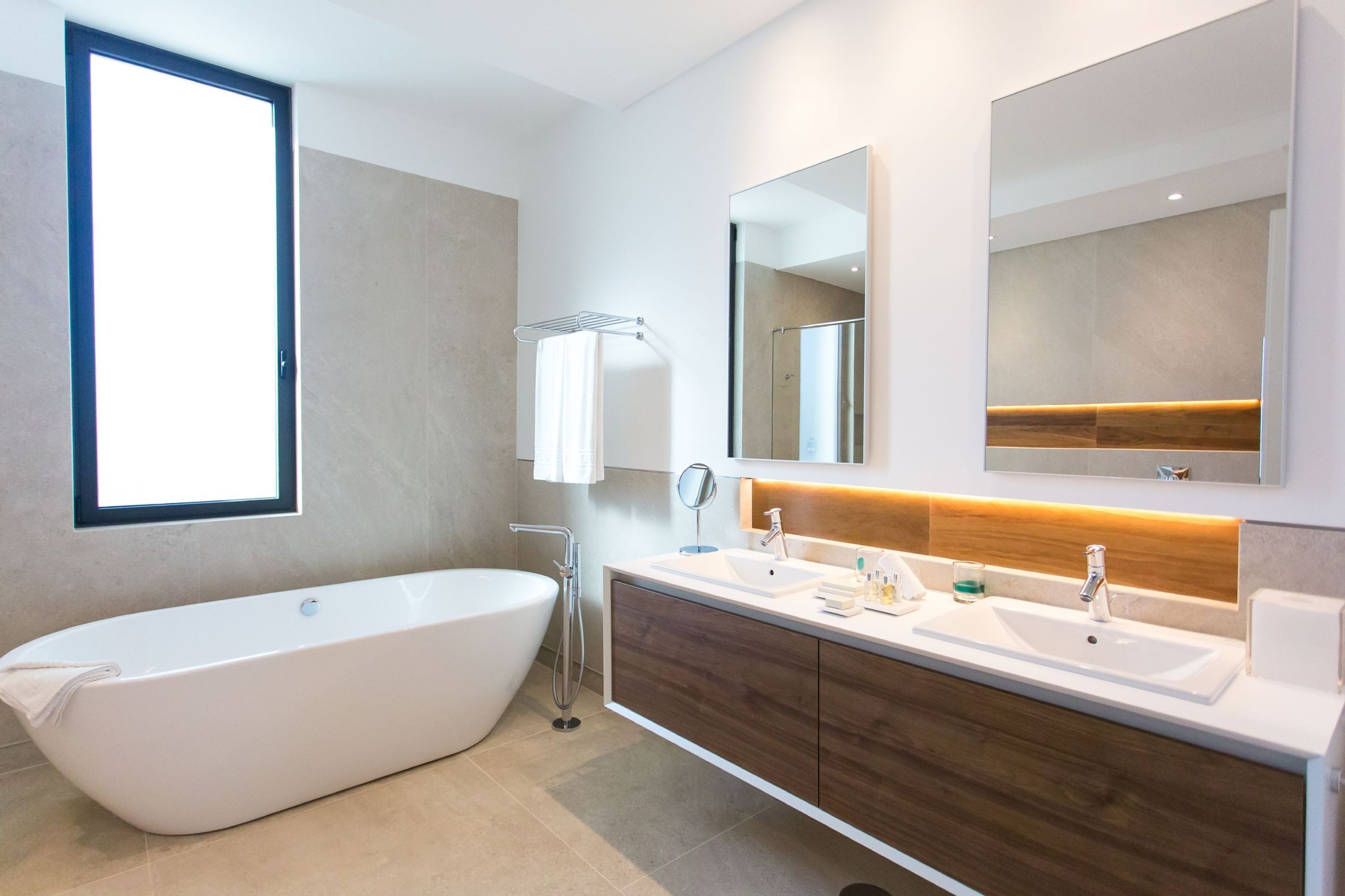 Une salle de bain moderne avec une baignoire sur pieds, deux lavabos, un grand miroir et une fenêtre.