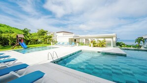 A swimming pool with lounge chairs, a slide, and a building with a white facade. - La Vista #601, brand New 3 bd Condo overlooking Tamarindo Bay (Playa Tamarindo)