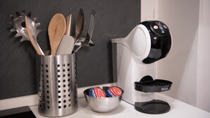 Una encimera de cocina con una cafetera, un recipiente para utensilios y un bol de cápsulas de café.