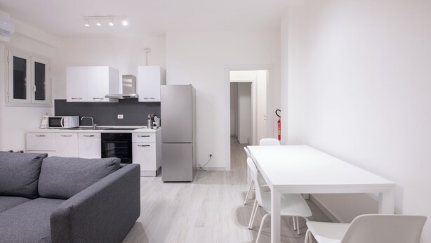 Una cocina moderna con armarios blancos, un sofá gris y una mesa de comedor blanca.