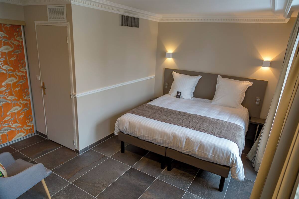 A bedroom with a bed, two bedside lamps, a chair, and a door with a patterned wallpaper.
