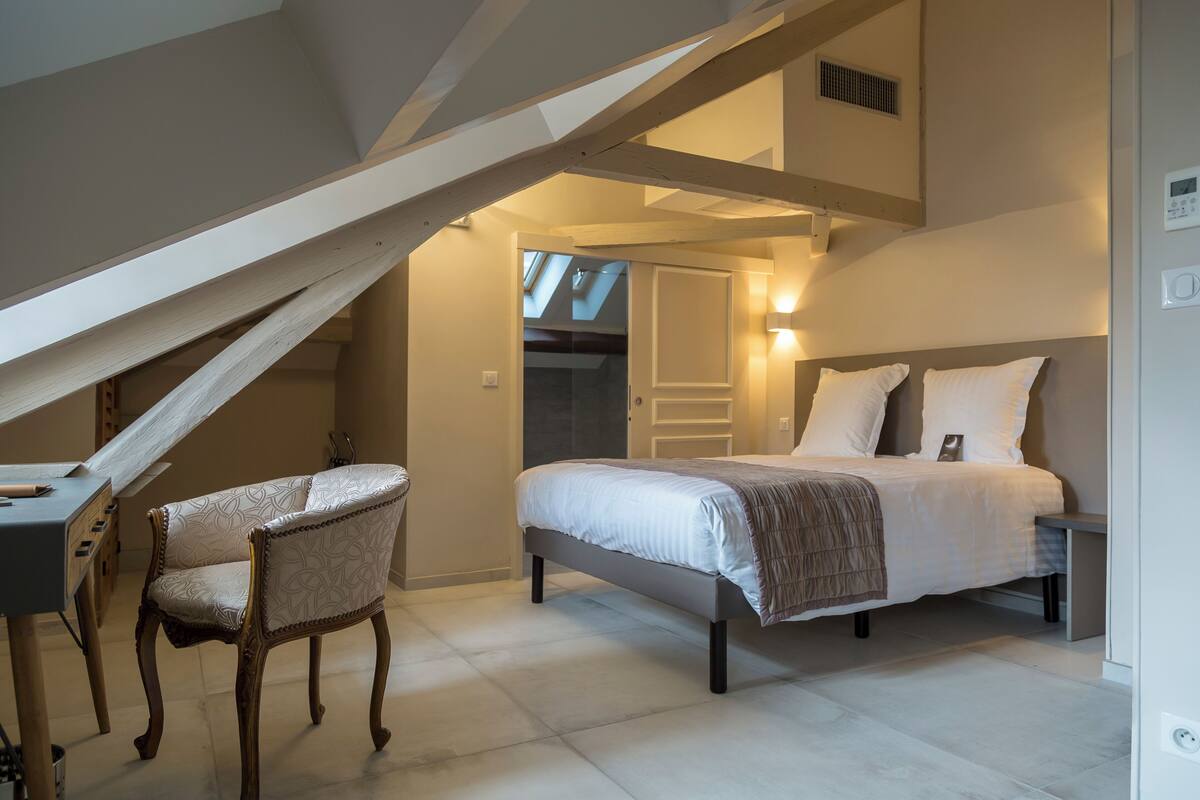 A bedroom with a bed, a chair, a desk, and a skylight.