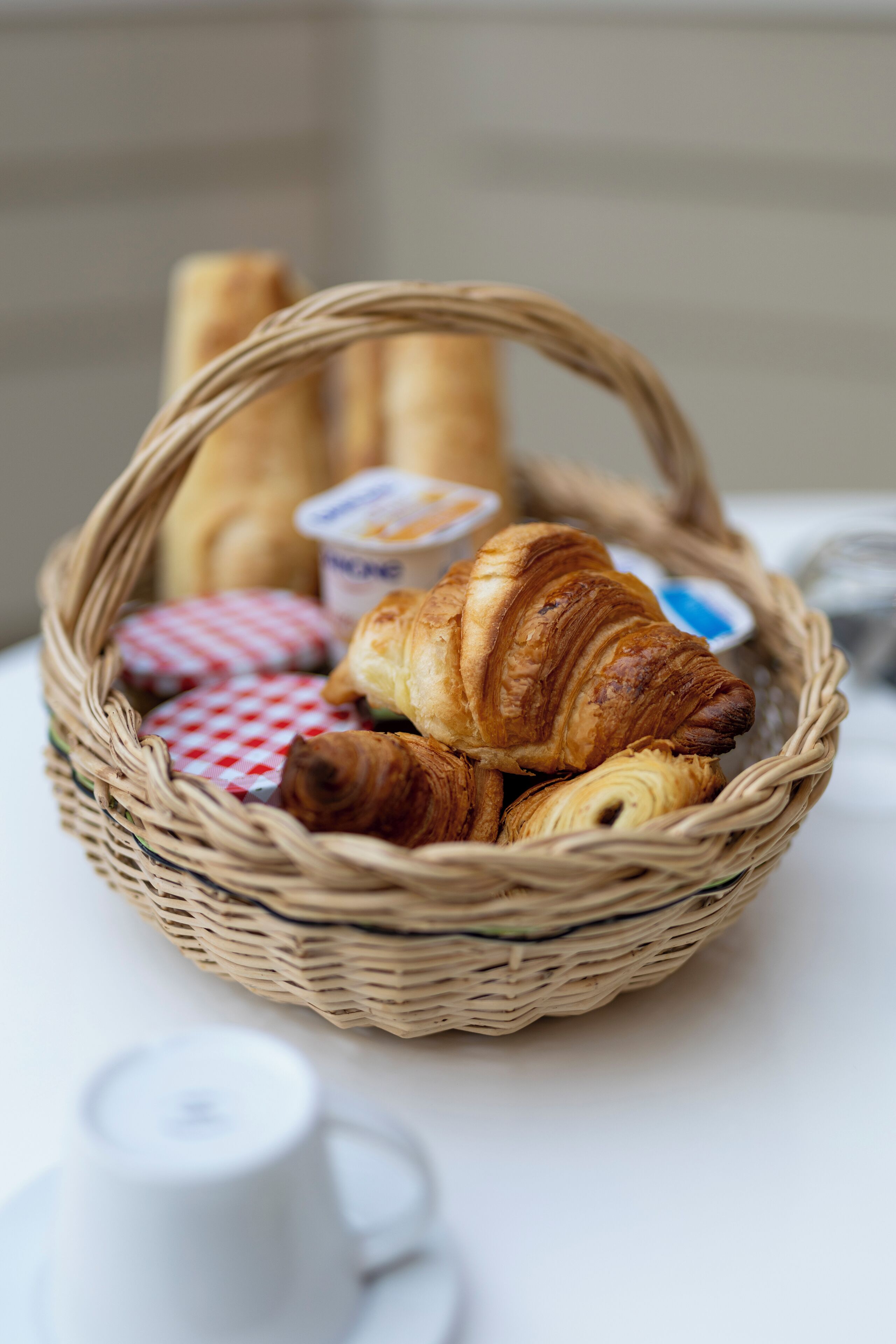A wicker basket containing croissants, a small container of butter, and a cup of coffee on a table.
