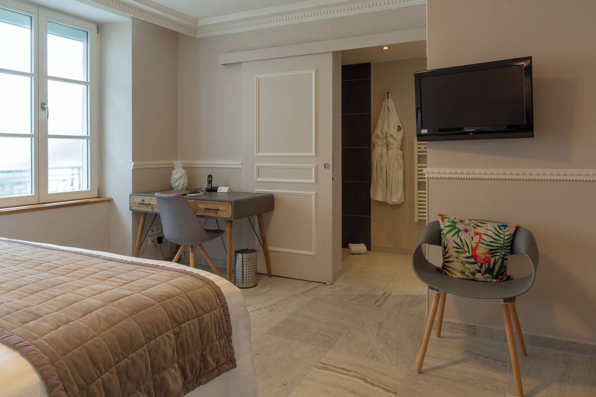 A hotel room with a bed, a desk, a chair, a television, and a bathroom visible through an open door.