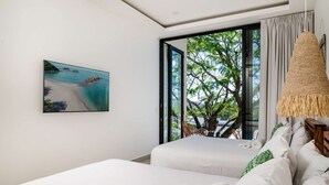 A modern hotel room with a large window offering a view of a beach and tree. There are two beds with white linens and a painting of a beach scene on the wall. - Luxury This 2-bed, 2-bath villa with Exclusive access to the Langosta Beach Club (Tamarindo)