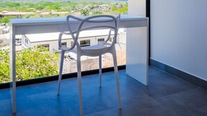 Ein Balkon mit weißem Stuhl, Blick auf die Landschaft und drei gewebte Wanddekorationen.