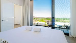 Ein Schlafzimmer mit einem großen Bett, zwei zusammenge rollten Handtüchern, Blick auf einen Balkon mit Gartenmöbeln und einer Tür links.