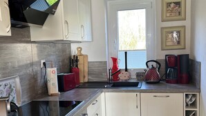 A compact kitchen with white cabinets, a built-in oven, a sink, and a window with blinds. - Reed-roofed FH with beach chair in the garden and close to the beach (Dranske)