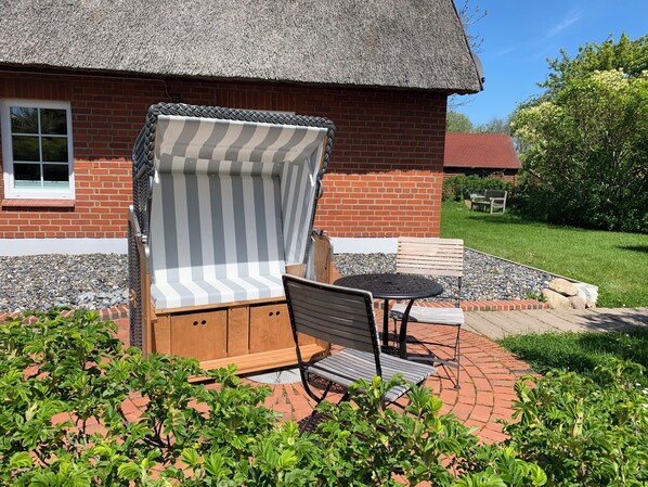 Un patio con una zona de estar al aire libre a rayas, un banco de madera y una mesa.