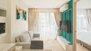 Una habitación de hotel moderna con sofá, televisión, cama y un ventanal con cortinas.