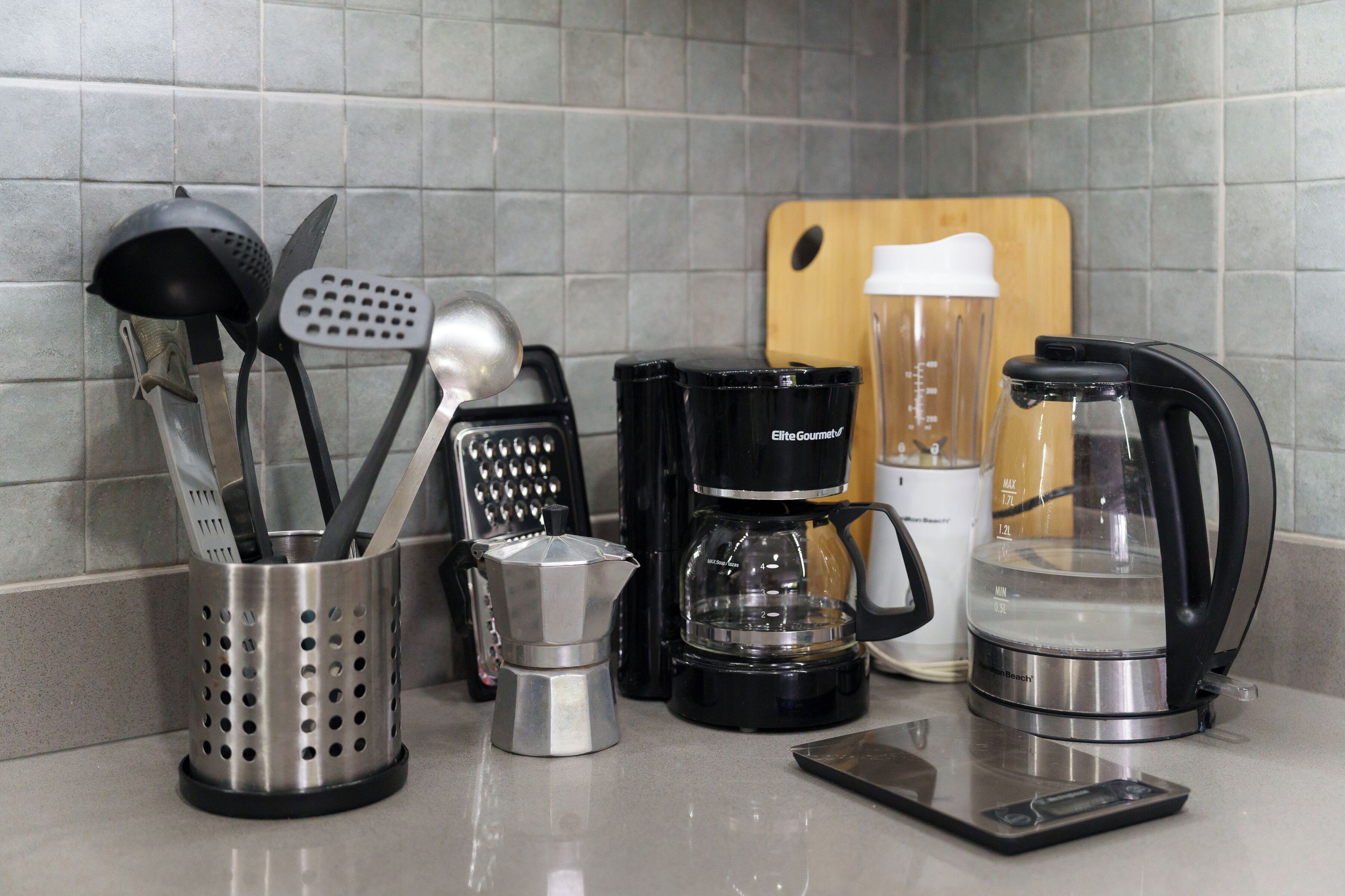 Uma bancada de cozinha com diversos eletrodomésticos, incluindo uma cafeteira, um liquidificador e uma chaleira.