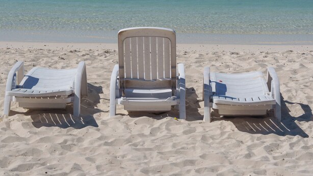 Three white beach chairs facing the ocean on a sandy beach.