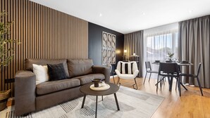 A modern living room with a sofa, coffee table, and dining area with chairs and a table. - London Grove Apartments (London)