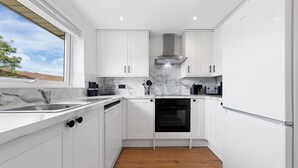 A modern kitchen with white cabinets, a marble countertop, a built-in oven, and a window with a view of the outside. - London Grove Apartments (London)