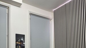 Ein kleines, modernes Zimmer mit einem Bett, einem Esstisch mit Stühlen und einem Fenster mit Jalousien.
