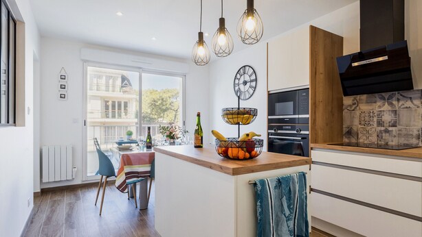 A modern kitchen with a wooden countertop, hanging pendant lights, and a view of a balcony.