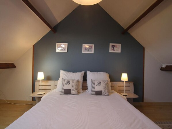 A bedroom with a sloped ceiling, a large bed with multiple pillows, two bedside tables with lamps, and three framed pictures on the wall.