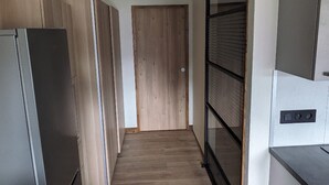 A narrow hallway with wooden flooring, a refrigerator on the left, and a sliding door on the right.