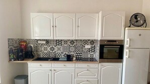 Eine kleine Küche mit weißen Schränken, einer gemusterten Spritzschutzeinrichtung, einem eingebauten Backofen und einem Kühlschrank.
