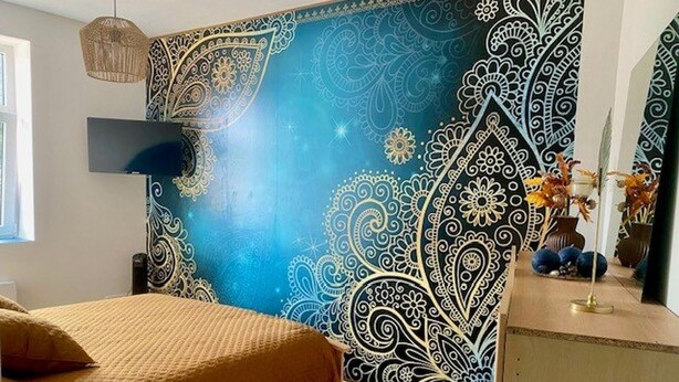 Ein Schlafzimmer mit einem großen Bett, einem an der Wand montierten Fernseher und einer Wand mit aufwendigen Mustern.