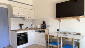 Eine kompakte Küche mit weißen Schränken, einem Einbauofen, einer Kaffeemaschine und einem flachbildfernseher an der Wand.