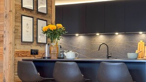 A modern kitchen with dark cabinets, a marble backsplash, and a central island with bar stools. - Spacious apartment in Les Gets, 4 bedrooms, sauna (Les Gets)