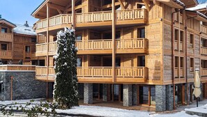 A multi-story wooden building with balconies, stone foundations, and a snow-covered tree in front. - Spacious apartment in Les Gets, 4 bedrooms, sauna (Les Gets)