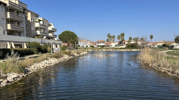 Une rivière traverse un quartier résidentiel, bordé d’un côté par de modernes immeubles d’appartements.