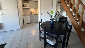 Une cuisine compacte équipée d’un four à micro-ondes, d’une cuisinière et d’un évier. Une table à manger avec des chaises se trouve au premier plan.