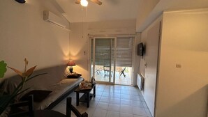 Une pièce dotée d’un ventilateur de plafond, d’une table avec des chaises, d’un banc et d’une porte-fenêtre coulissante donnant sur un espace extérieur.