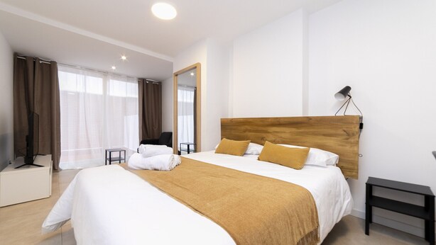 Een moderne hotelkamer met een groot bed, een houten hoofdbord, een nachtkastje en een spiegel aan de muur.