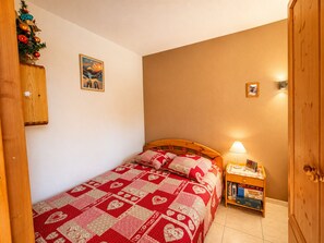 A bedroom with a wooden bed, a nightstand, a lamp, a small shelf with books, and a Christmas decoration.