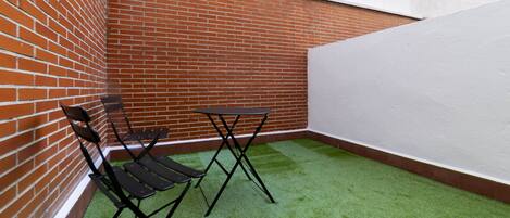 A small, enclosed outdoor area with artificial green turf, a brick wall, and a white wall.
