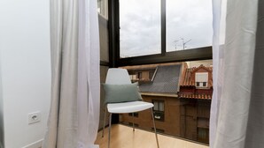 Une pièce avec une fenêtre, une chaise et une vue sur les bâtiments à l’extérieur.