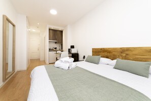 A hotel room with a large bed, a wooden headboard, a kitchenette, and a bathroom visible through an open door. - Luxury IV - Ferga Suites (Madrid)