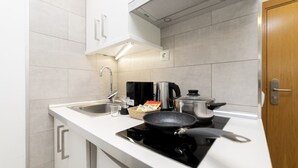Une cuisine moderne avec des meubles blancs, une cuisinière noire, une machine à café et une bouilloire.
